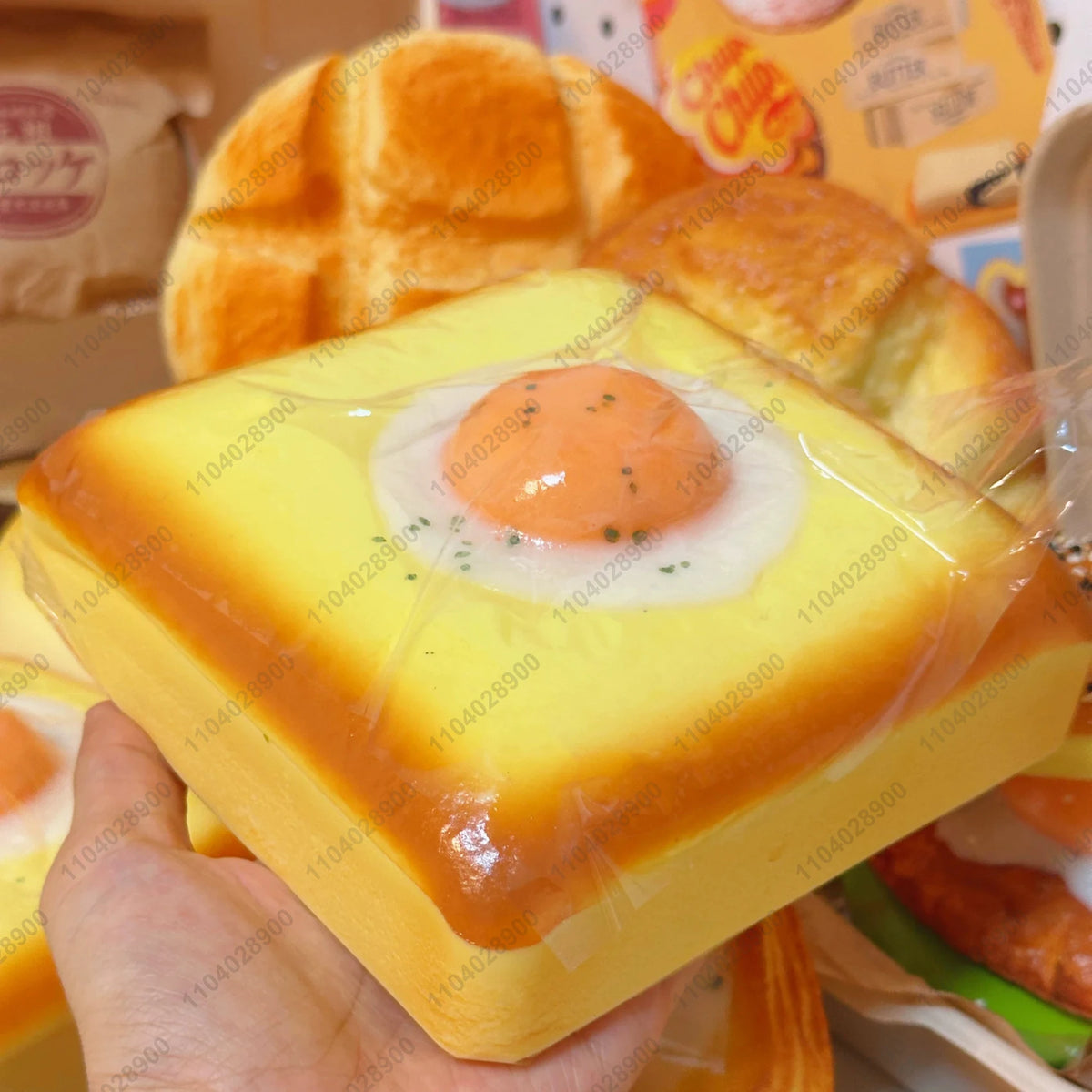 A hand holds a yellow squishy fried egg toast stress relief toy next to a loaf of bread.