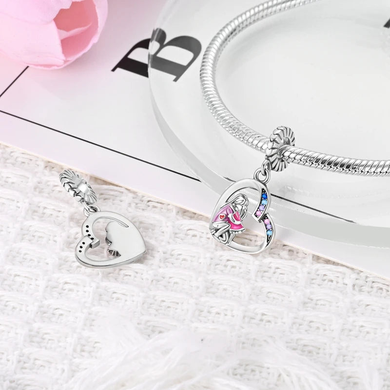 A silver heart charm for bracelets and necklaces is displayed next to a silver chain on a white surface.