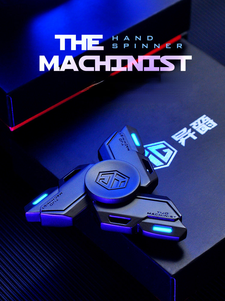 A close-up of a blue metal luminous fidget spinner resting on a dark surface with the title The Machinist visible in the back