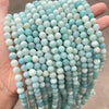 A hand holds a string of light blue and white natural amazonite beads for jewelry making