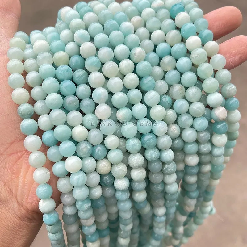 A hand holds a string of light blue and white natural amazonite beads for jewelry making