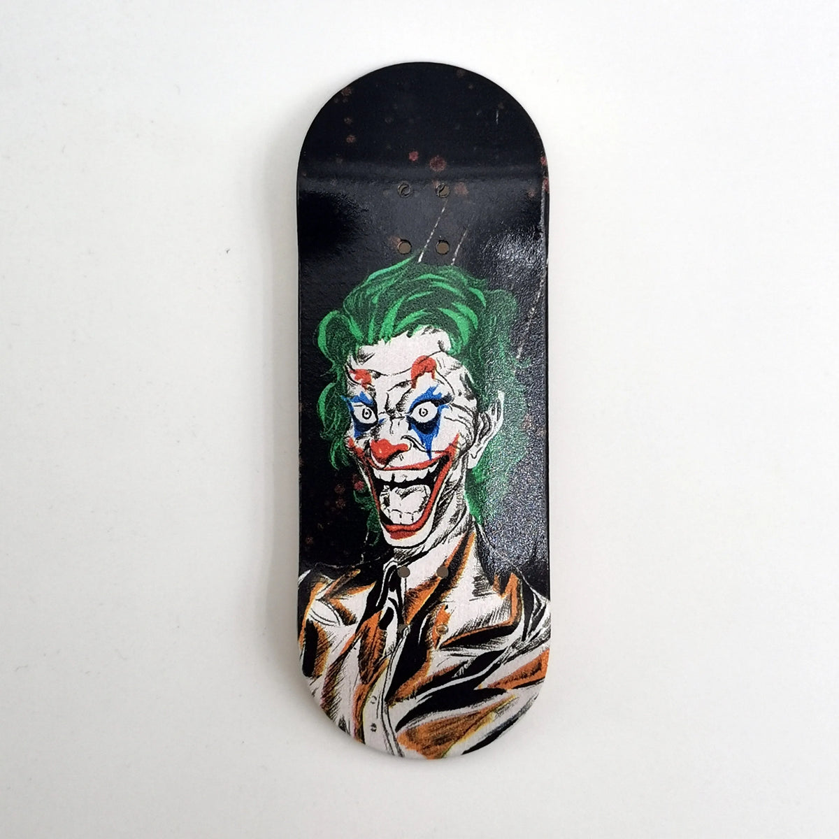 A black wooden fingerboard deck featuring a UV-printed graphic of the Joker face.