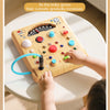 A child is interacting with a wooden early education board featuring various lights and switches for sensory exploration.