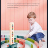 A young boy is playing with an automatic domino train toy made of colorful building blocks on a white floor.