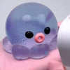 A translucent purple octopus squishy stress ball with black eyes and a pink nose is held in a hand.