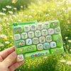 A hand holds a green keyboard keycap set featuring various cartoon animal and food icons for stress relief.