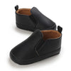A pair of black baby first walker sneakers with a textured pattern and brown lining.