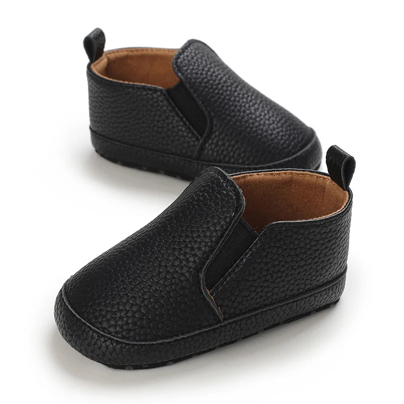 A pair of black baby first walker sneakers with a textured pattern and brown lining.