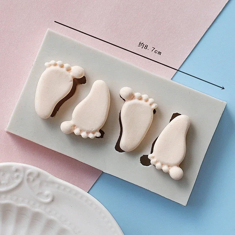 A set of white silicone baby-themed cake molds including a stroller, bottle, and pacifier on a light pink background.