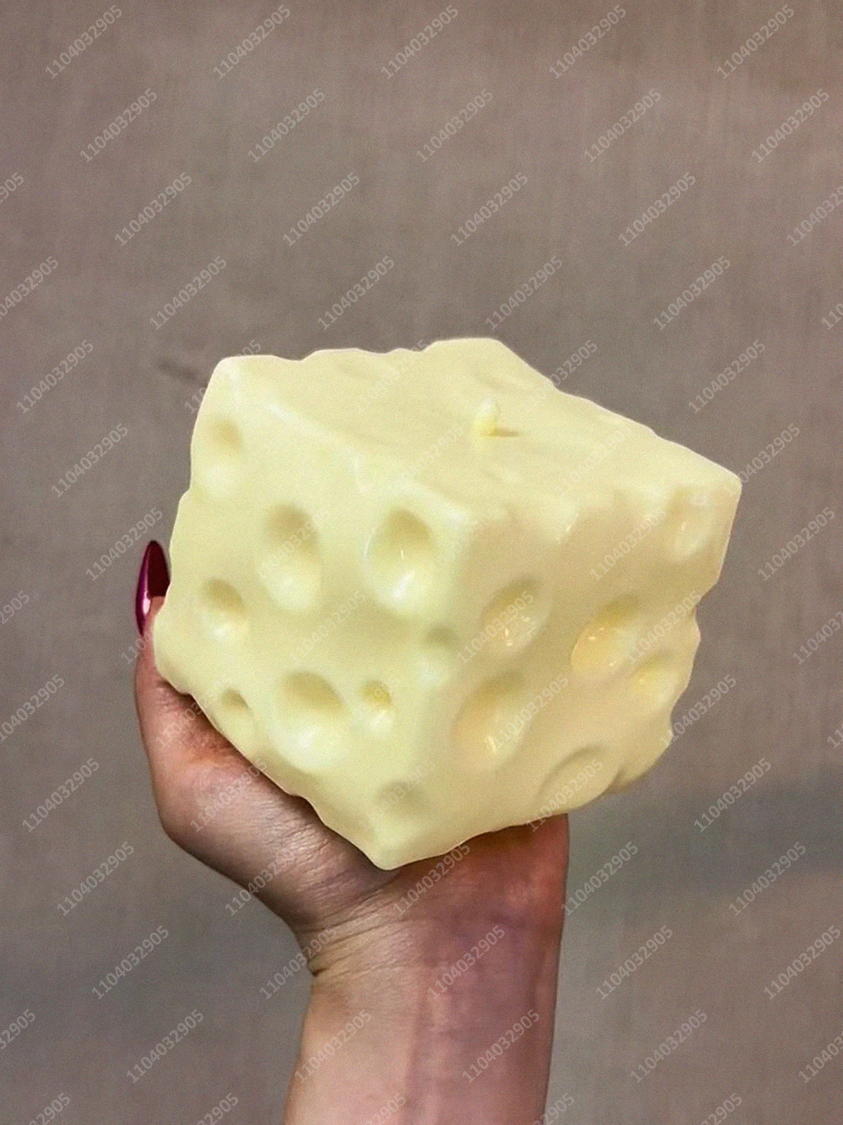 A hand holds a large, pale yellow cheese cube stress ball against a neutral background.