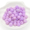 A pile of small, round, purple acrylic pearl beads in a white dish for jewelry making.