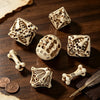 A set of bone skull carved polyhedral dice and a quill pen resting on dark wood.