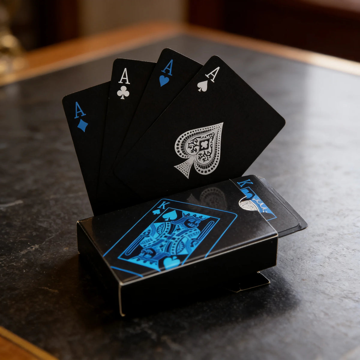 A stack of black playing cards, including aces and kings, rests on a dark surface.