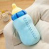 A light blue milk bottle plush pillow with a yellow cap resting on a beige fabric surface.
