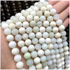 A close-up of numerous natural stone beads in white, pale green, and translucent shades arranged on a hand.