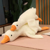 A white plush goose pillow with orange beak and feet lying on a pink surface.