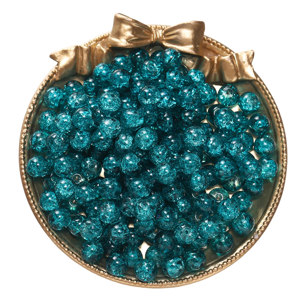 A round gold-toned dish filled with bright teal blue glass crackle beads for jewelry making
