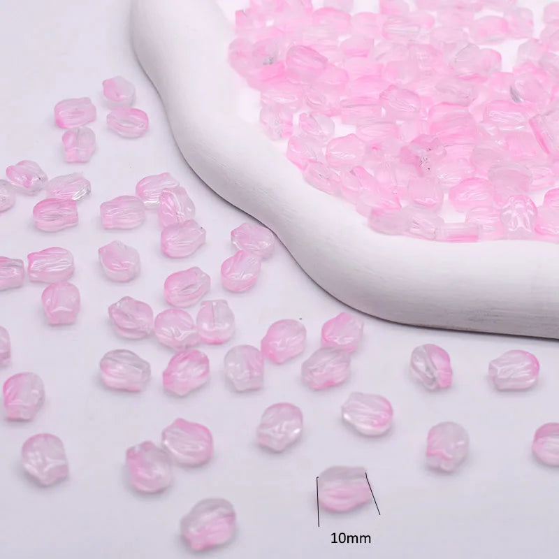 Pink gradient tulip glass beads scattered next to a white ceramic tool for jewelry making