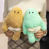A person holds a yellow monster plush doll with white pants and a green monster plush doll.