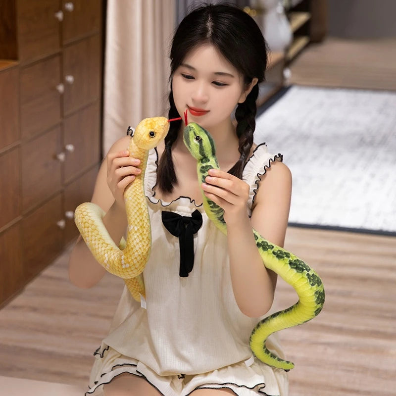 A young woman is holding a lifelike simulation snake plush toy with yellow and green coloring.