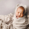 A newborn baby sleeping wrapped in a light knit fabric with a pearl headband.
