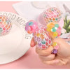 A hand holds a colorful, translucent squishy stress relief ball with various mixed colors on a white plate.