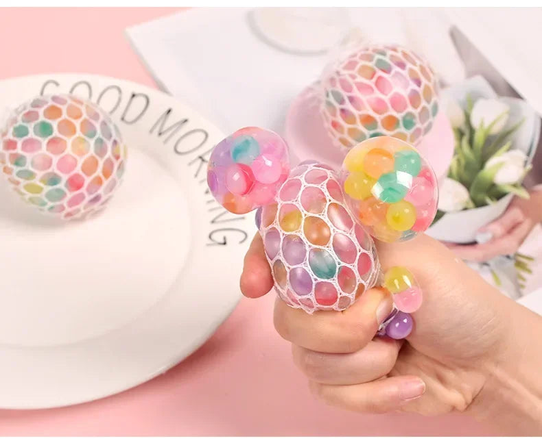 A hand holds a colorful, translucent squishy stress relief ball with various mixed colors on a white plate.