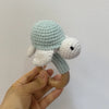 A hand holds a light blue and white wooden baby rattle and teether ring shaped like an otter.