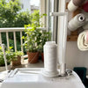 A white vertical sewing machine spool holder with a thread guide is shown on a white machine.