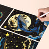 A hand is writing on a piece of glow-in-the-dark scratch art featuring a whale against a moon and starry background.