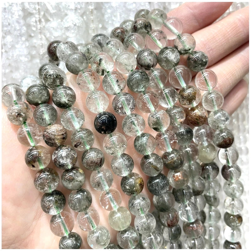 A hand holds multiple strands of natural stone beads including amethyst, garnet, and labradorite for jewelry making.