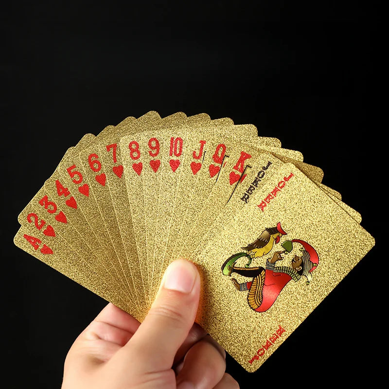 A hand holds a fan of gold glitter poker playing cards with red hearts and jacks.