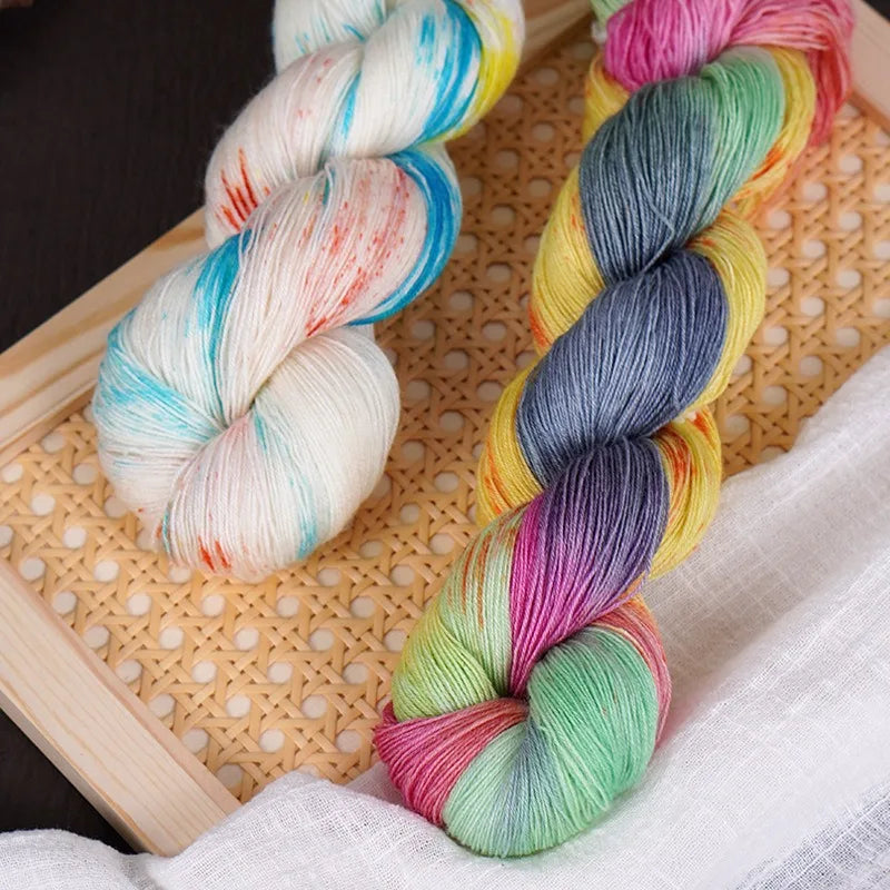 A skein of hand-dyed Australian wool yarn with a vibrant gradient of colors is shown coiled on a light wooden mat.