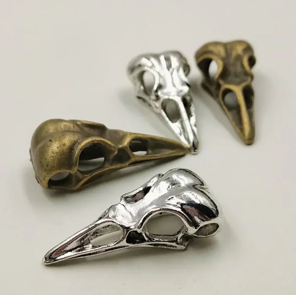 A collection of silver and bronze gothic skull bird head pendants displayed on a white background.