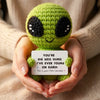 Handmade crochet alien plush toy with green skin and black eyes is held in a person's hands.