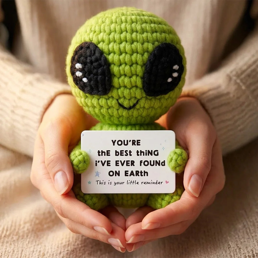 Handmade crochet alien plush toy with green skin and black eyes is held in a person's hands.