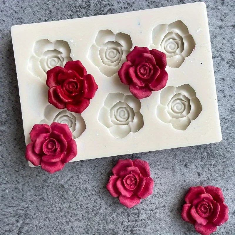 A white silicone mold with five pressed rose flower cavities, some filled with deep pink or magenta colored material.