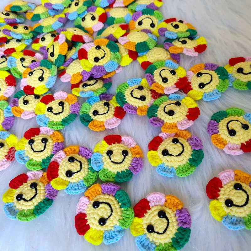 A collection of handmade crochet sunflower decorative smile orbs in various bright colors scattered on a white surface.