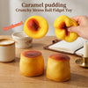 A hand holds a yellow caramel pudding stress ball fidget toy next to other similar toys on a wooden surface.