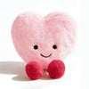 A pink, heart-shaped plush cushion with embroidered features and red feet.