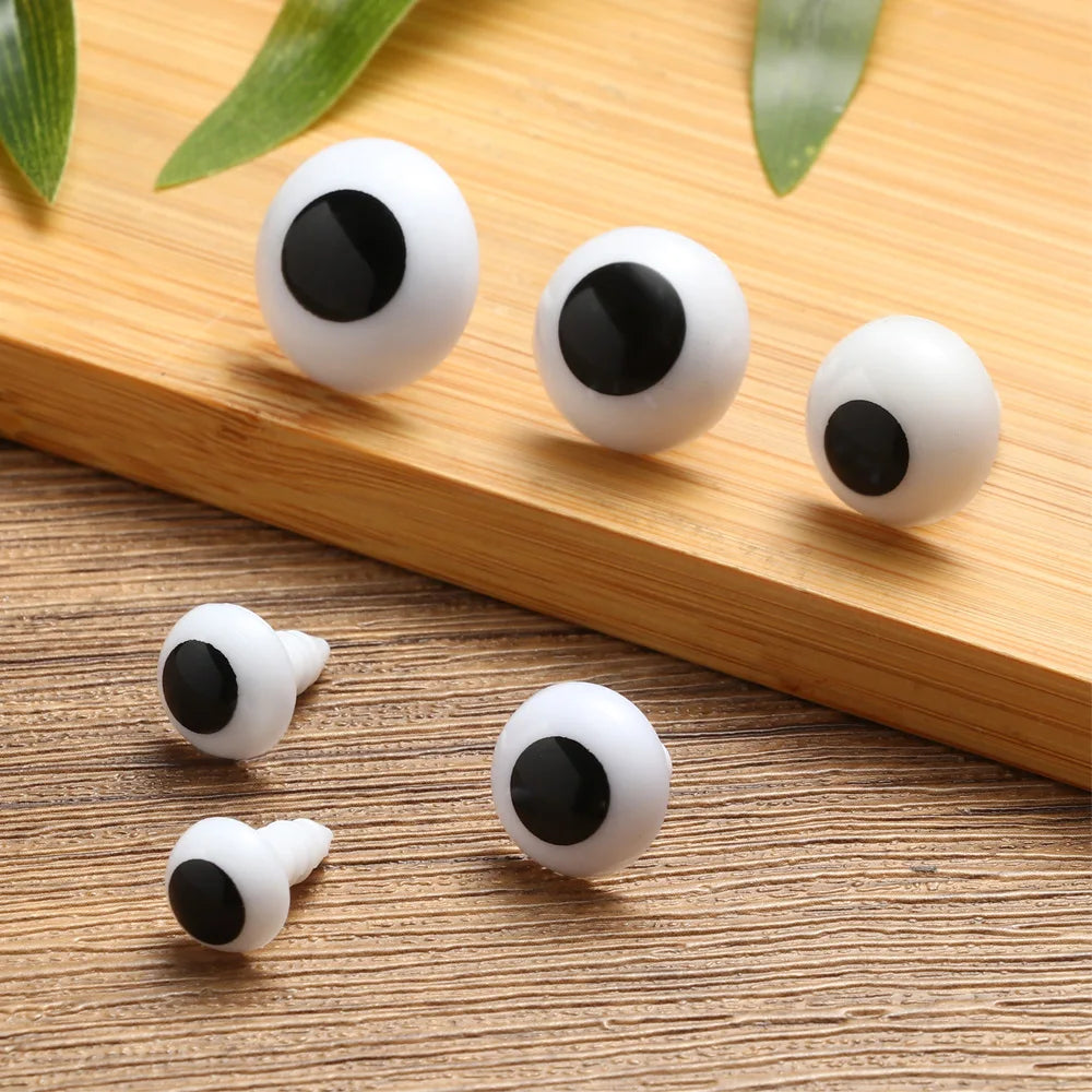 Several white plastic safety eyes with black pupils are arranged on a wooden surface.