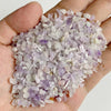 A hand holds a pile of light purple and clear quartz stone chips for jewelry making