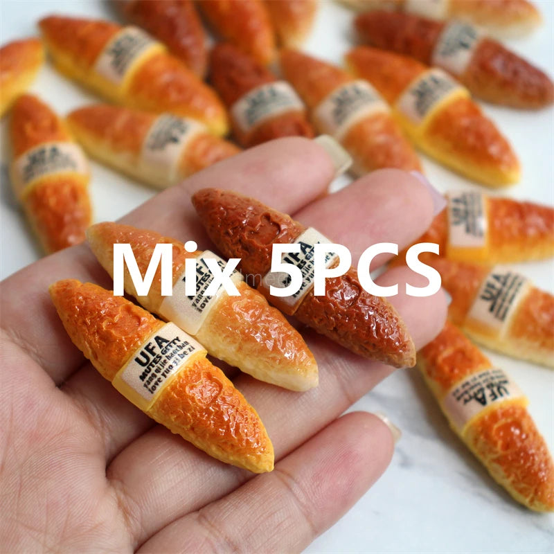 A hand holds five miniature baguette-shaped items, likely food or decorative, on a white surface.