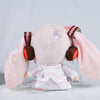 A pink Hatsune Miku plush doll with large ears and a white outfit is displayed against a light gray background.