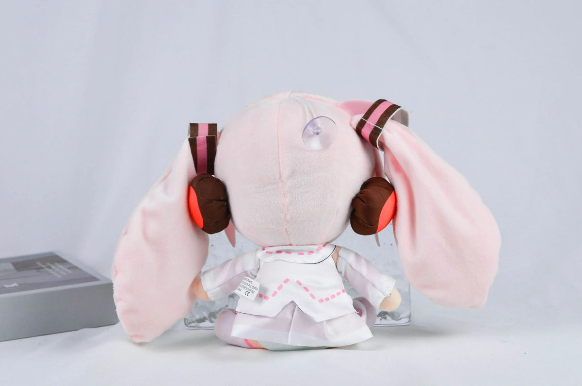 A pink Hatsune Miku plush doll with large ears and a white outfit is displayed against a light gray background.