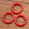 A set of ten red metal O-ring spring clasps for DIY jewelry and keychains resting on a wooden surface.