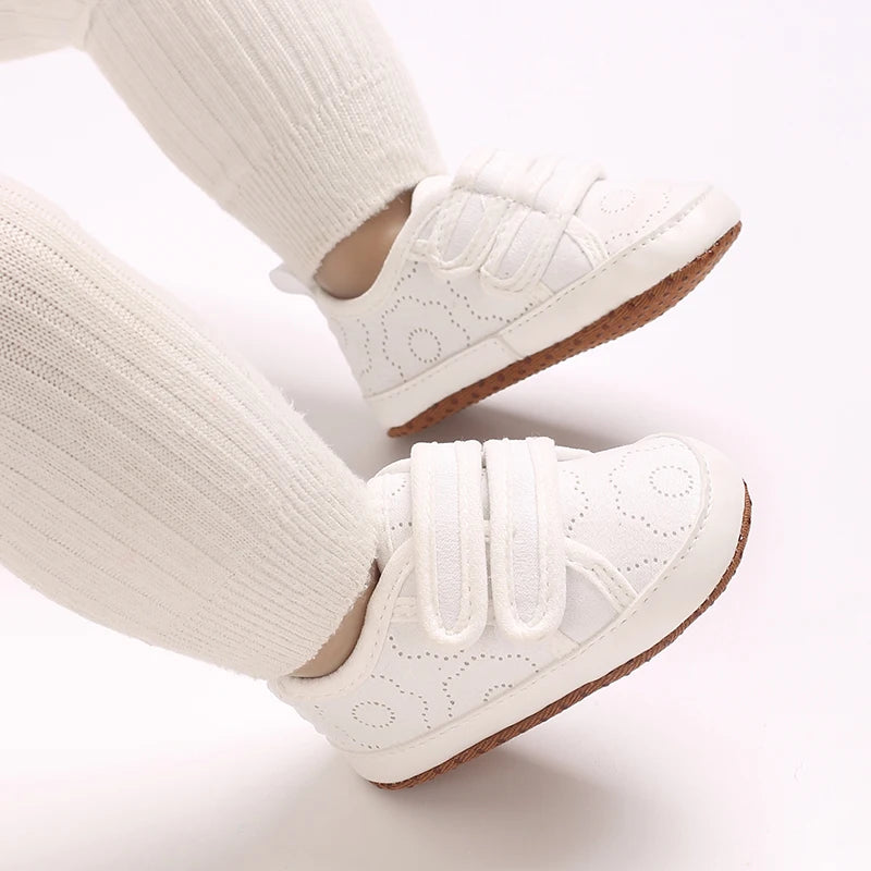 A pair of classic white soft-sole baby first walkers with knit socks shown from the side.