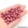 A handful of pink rhodonite round beads for jewelry making resting on a hand.