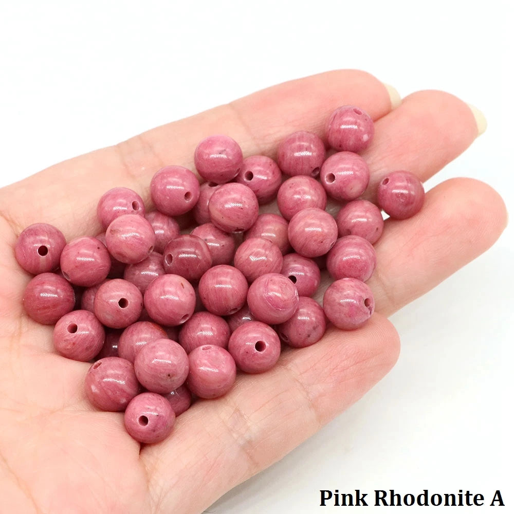 A handful of pink rhodonite round beads for jewelry making resting on a hand.
