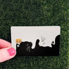 A black cat silhouette with whiskers and a paw print is printed on a white card against a green background.
